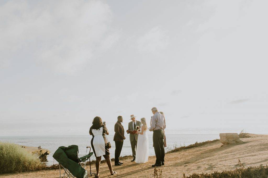 Couple stands on Sunset Cliffs with their officiant and a few guests.