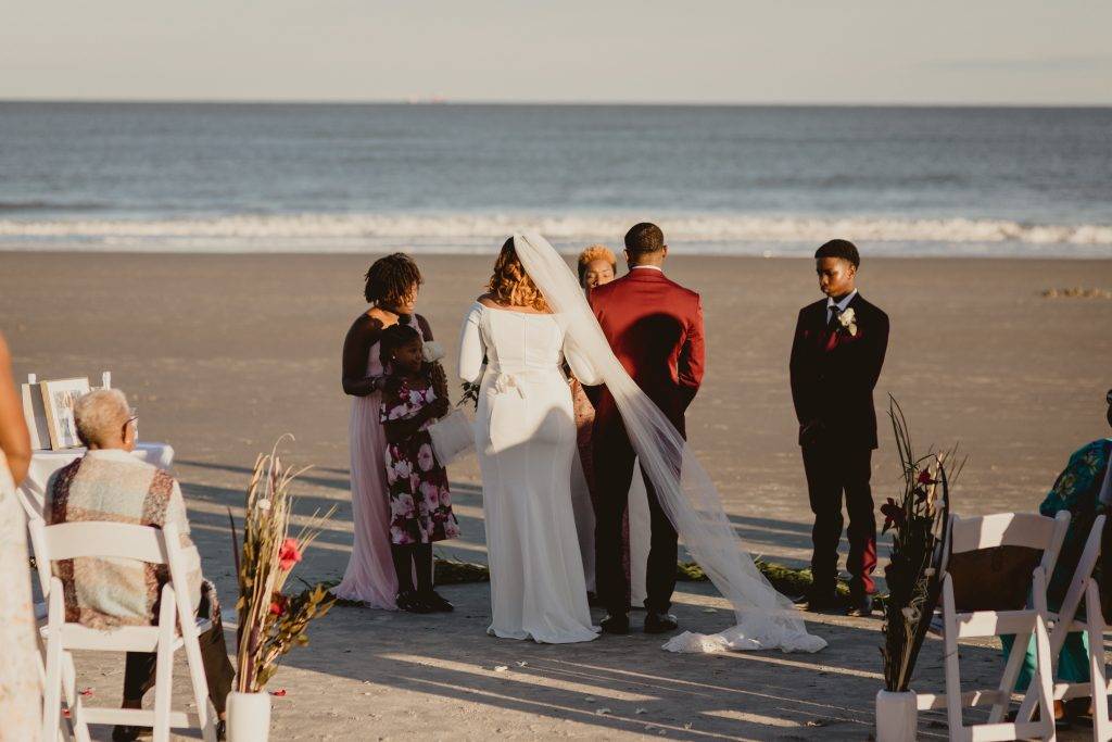 Couple walks down the aisle between white chairs on Tybee Island beach towards their officiant.