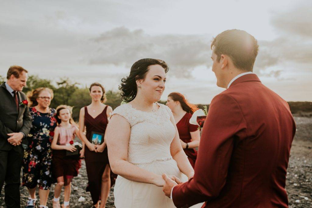 Couple holds hands while exchanging vows during their elopement ceremony with their guests behind them holding photos of the couple.