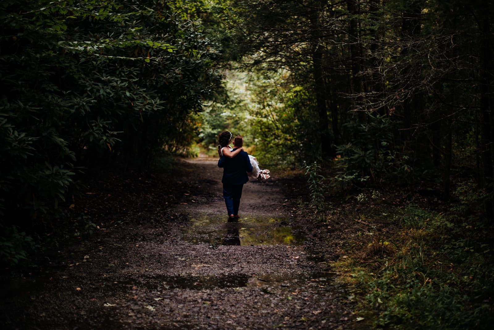 A groom carrying his bride among the trees of Pigsah National Forest.
