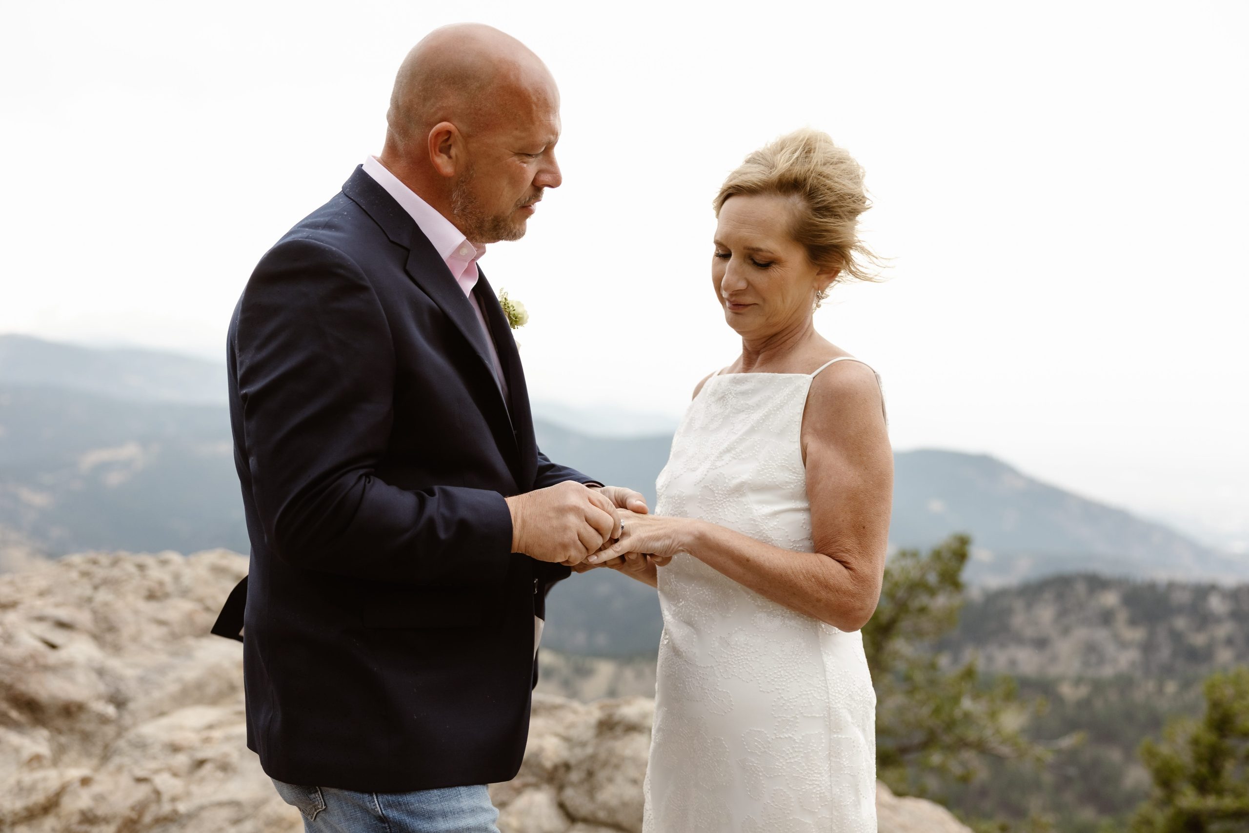 An intimate ring exchange on a rocky mountain overlook, showcasing why do couples elope for breathtaking views and a private connection with nature.