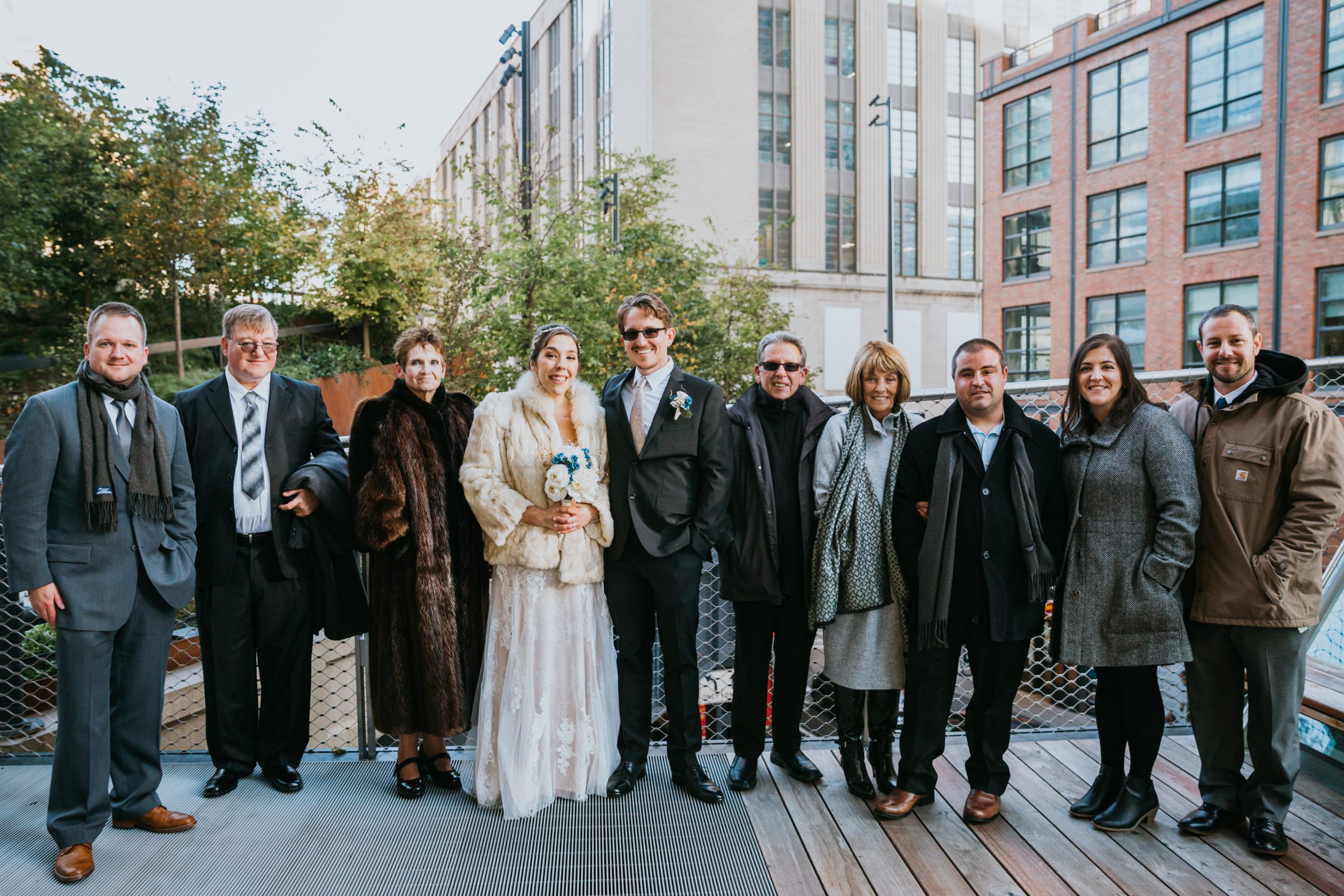 A wedding party and guests posing outdoors in New York City wearing various winter wedding guest outfits, including fur coats, wool overcoats, and heavy scarves to stay warm.
