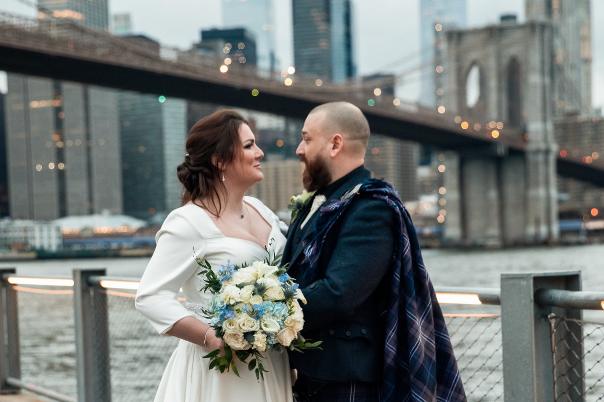 Couple embraces in view of the Brooklyn Bridge after their New York winter wedding.
